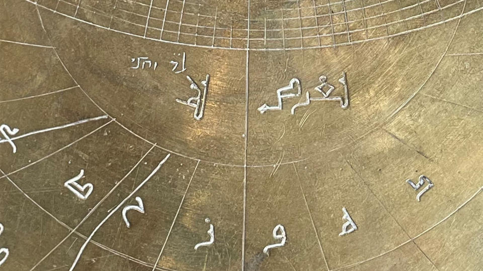 A close-up view of a bronze astronomy instrument showing Arabic and Hebrew signs.