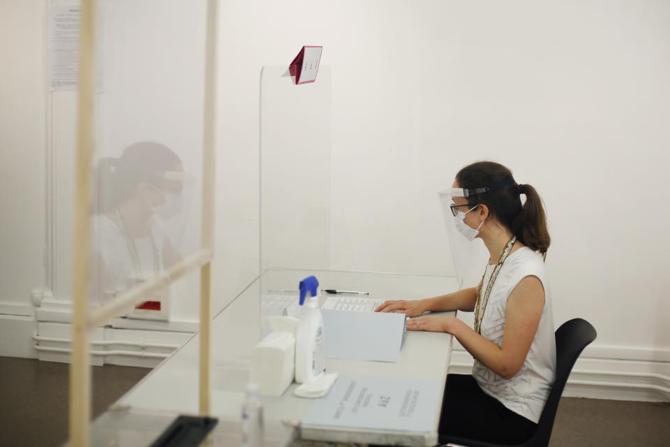 A woman wearing a face mask and visor to protect against coronavirus sits behind a glass shield during a rehearsal of the vote for the local elections scheduled for Sunday, June 28, in Paris, Friday, June 26, 2020. France is to hold its Covid-19 delayed second round of local elections on June 28. (AP Photo/Thibault Camus)