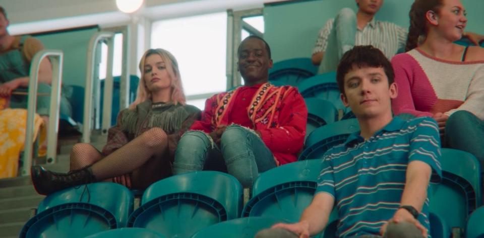 Otis, Maeve, and Eric sitting in the stands of their school's pool room in "Sex Education"