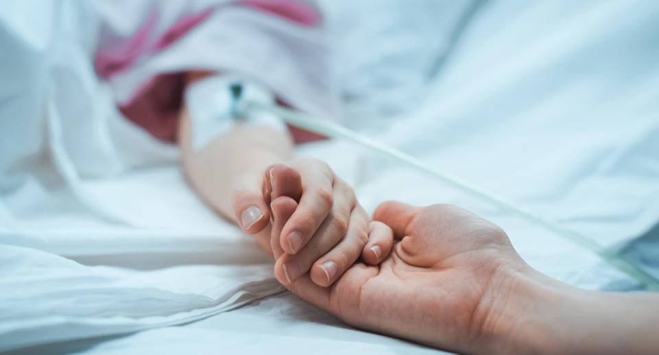 Two people hold hands in a hospital bed.