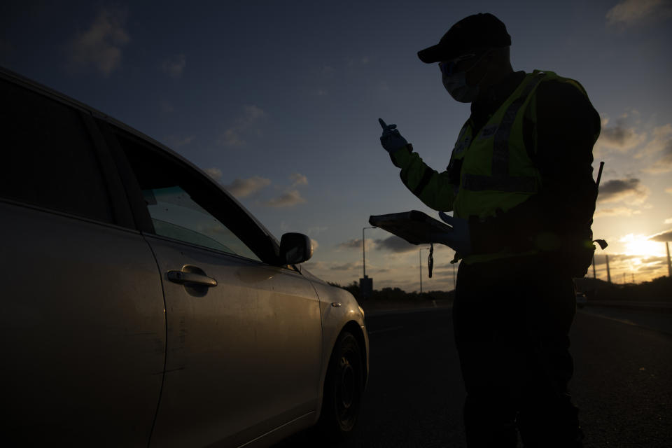 An Israeli police officer wears a face mask amid concerns over the country's coronavirus outbreak, as he checks the documents of a driver at a checkpoint on a freeway near Hadera, Israel, Tuesday, April 28, 2020. Israel's government announced a complete lockdown over the upcoming Israel's 72nd Independence Day to control the country's coronavirus outbreak. (AP Photo/Ariel Schalit)