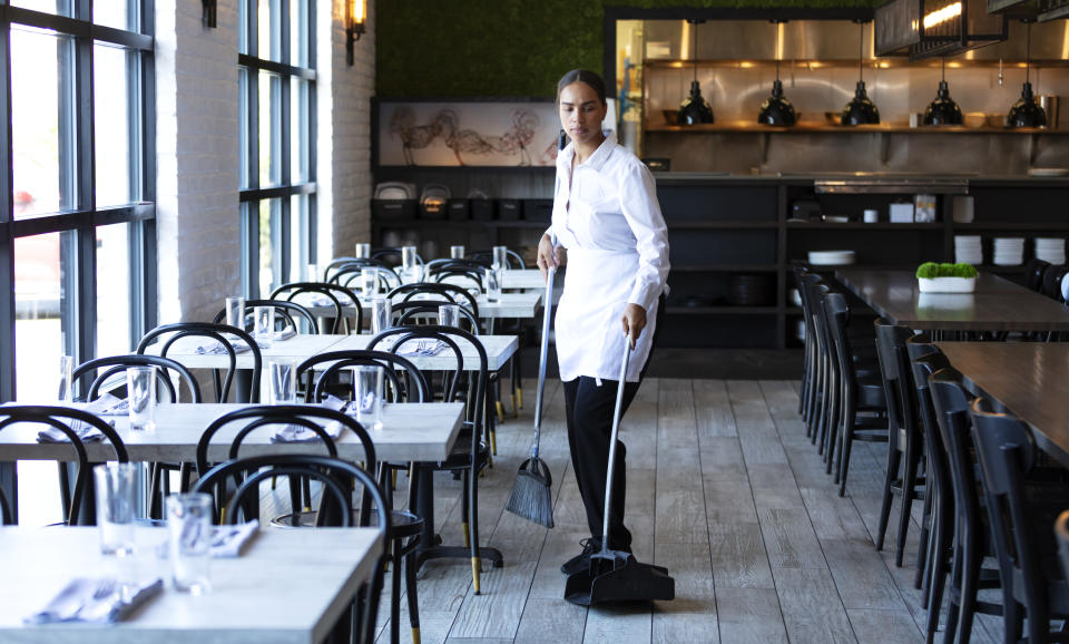 A worker sweeping the floor in an empty restaurant.