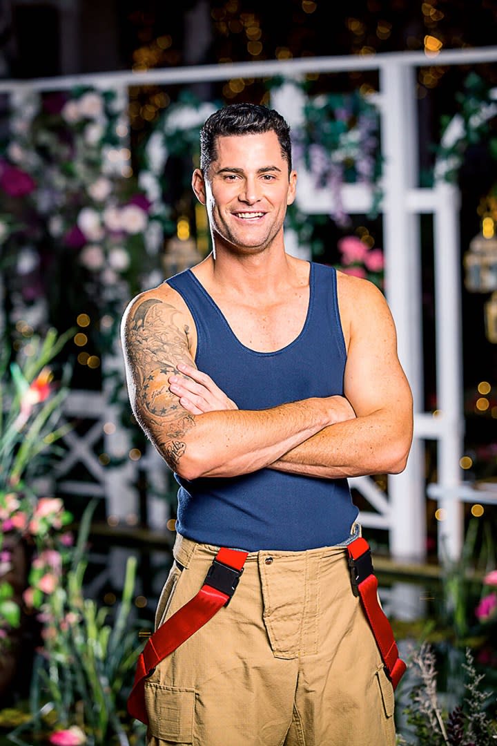 Bachelor In Paradise season three cast member Jamie Doran wearing a blue singlet and firefighter's trousers