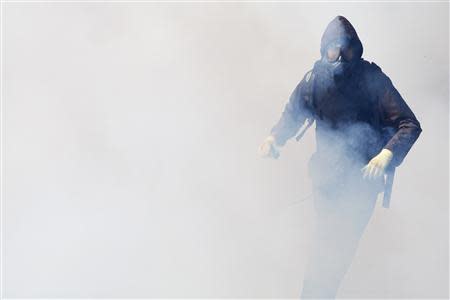An anti-government protester runs through a cloud of teargas during clashes with police near the Government House in Bangkok December 1, 2013. REUTERS/Kerek Wongsa