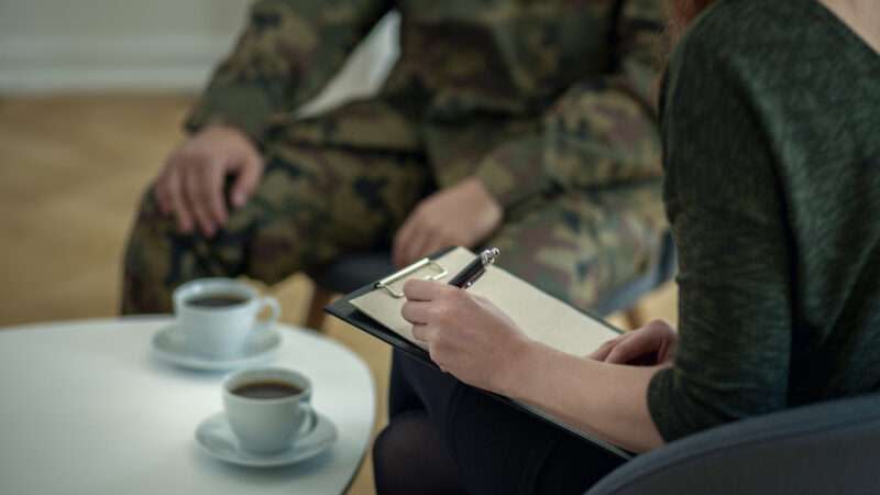 A soldier in military fatigues sits with a therapist.