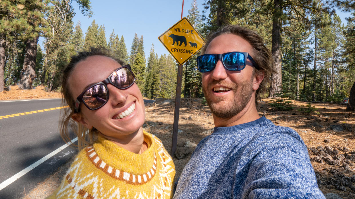  Couple taking selfie on road by 'wildlife crossing' sign. 