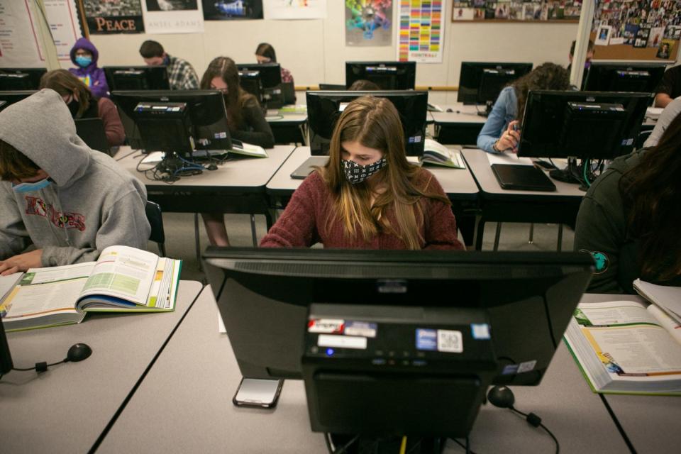 Students in masks complete schoolwork with computers and books.