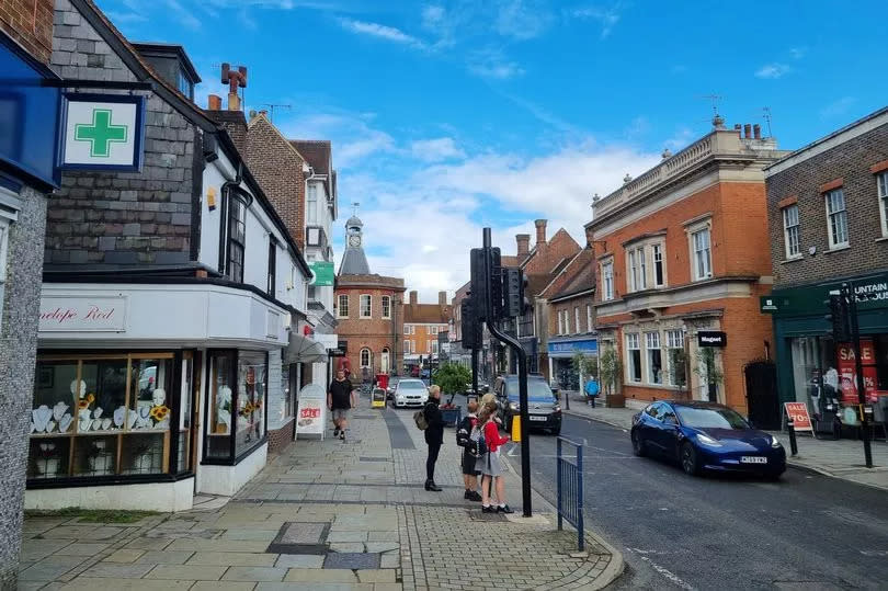 A view of Reigate's busy high street. There are lots of people and shops and vehicles.