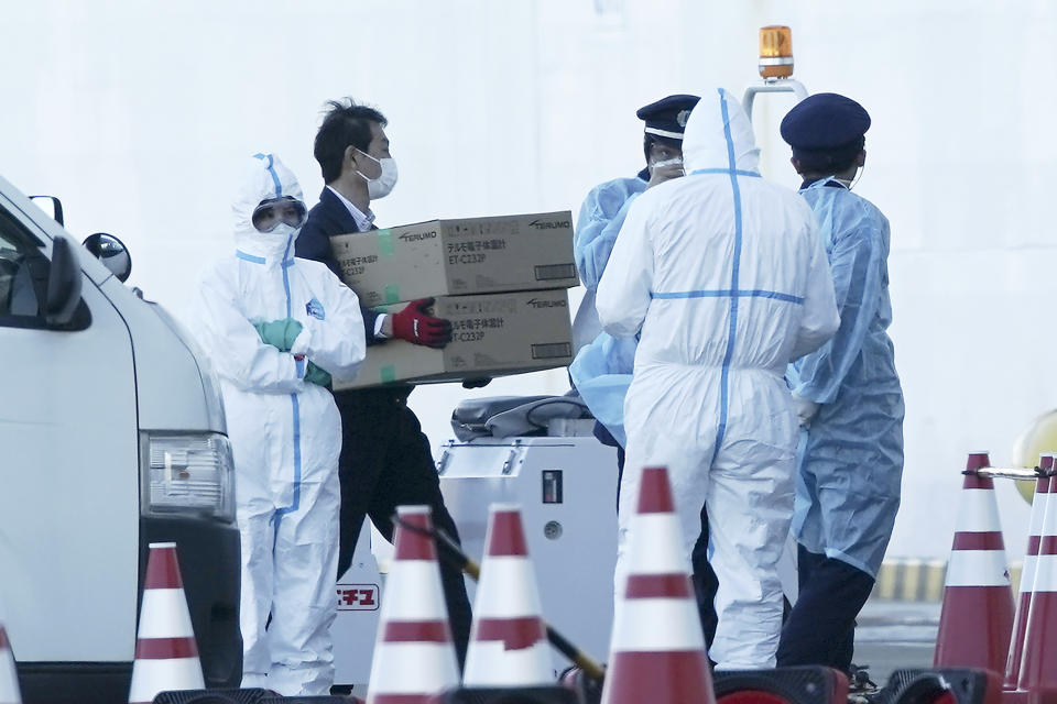 A masked official carry boxes containing digital thermometers for the cruise ship Diamond Princess anchored at Yokohama Port in Yokohama, south of Tokyo, Thursday, Feb. 6, 2020. The 3,700 people on board faced a two-week quarantine in their cabins. Health workers said 10 more people from the Diamond Princess were confirmed sickened with the virus, in addition to 10 others who tested positive on Wednesday. The 10 will be dropped off as the ship docks and transferred to nearby hospitals for further test and treatment. (AP Photo/Eugene Hoshiko)
