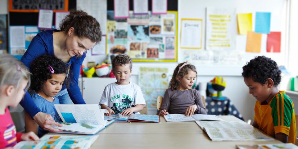 A teacher stands over a group of young students.