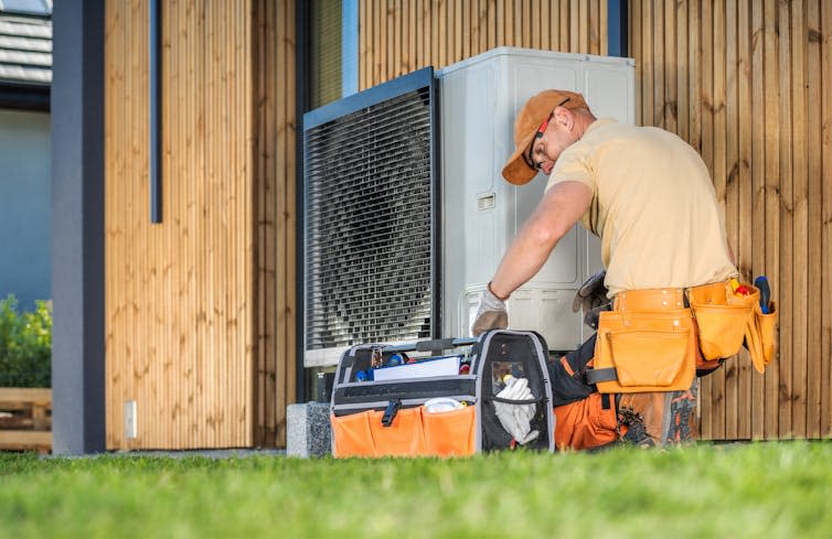 man fitting a heat pump to a home