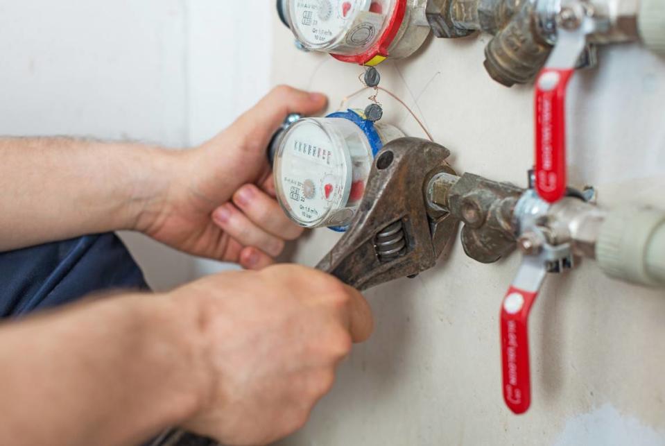 Male plumber fixing water meter with adjustable wrench.