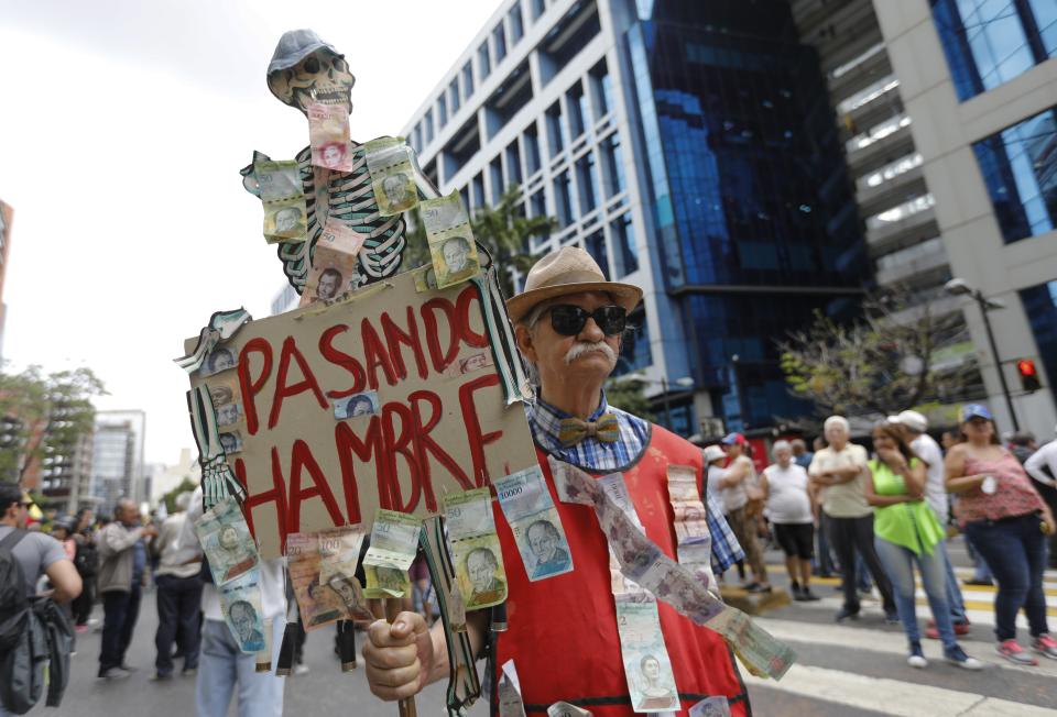 A protester carries sign with the Spanish message "Going hungry" during an opposition march in Caracas, Venezuela, Tuesday, March 10, 2020. U.S.-backed Venezuelan political leader Juan Guaido led the march aimed at retaking the National Assembly legislative building, which opposition lawmakers have been blocked from entering, but the march was blocked by police early in its route. (AP Photo/Ariana Cubillos)