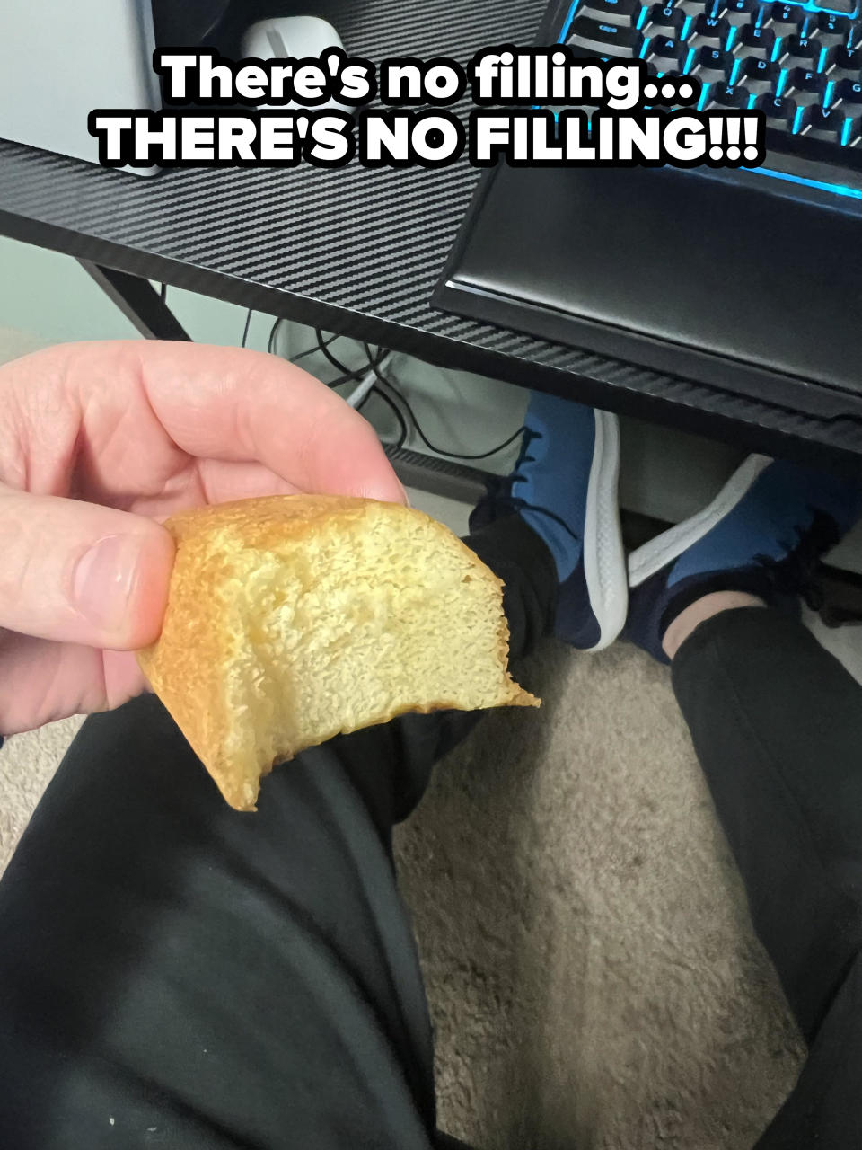 Person holding a half-eaten piece of toast with computer and legs in background