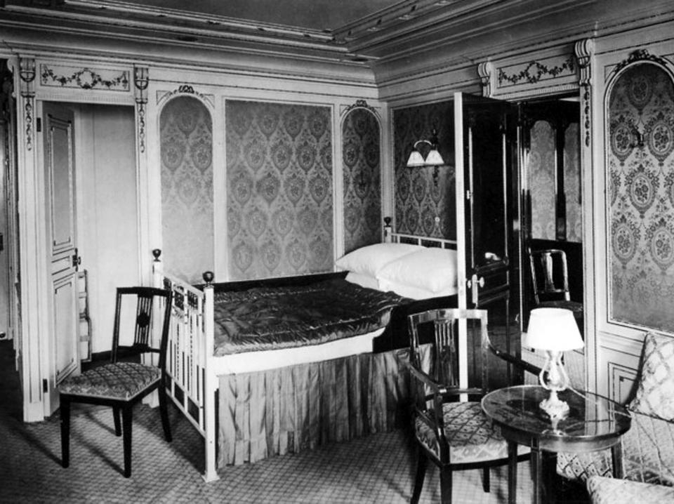 A black-and-white image of a cabin bedroom on the Titanic that has a large four-poster bed and a small seating area.