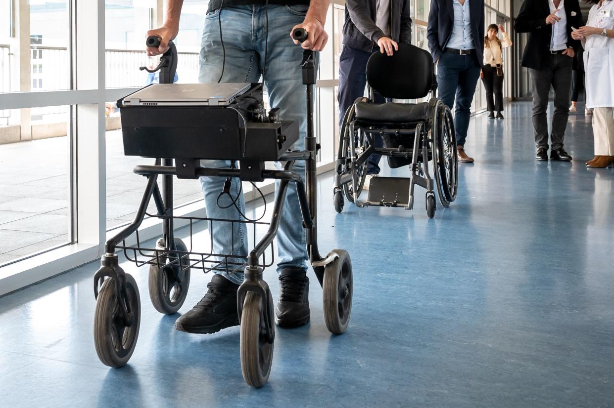 Oskam walks down a hallway while holding on to a wheeled walker.