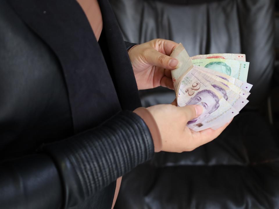 Hands of a woman holding Singaporean dollar banknotes, illustrating the findings of the Singlife Financial Freedom Index 2023 survey.