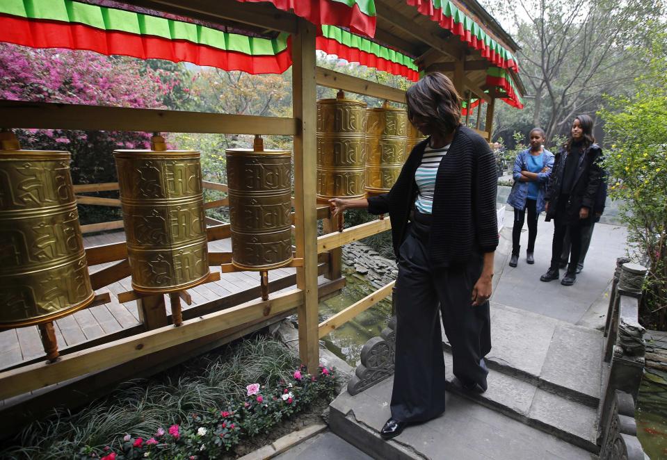 U.S. first lady Michelle Obama (L) touches Tibetan prayer wheels as her daughters Malia (R) and Sasha watch, outside a Tibetan restaurant in Chengdu, Sichuan province, March 26, 2014. (REUTERS/Petar Kujundzic)