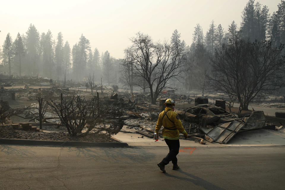 FILE - In this Friday, Nov. 16, 2018, file photo, a firefighter searches for human remains in a trailer park destroyed in the Camp Fire, in Paradise, Calif. Pacific Gas and Electric says it has reached a $13.5 billion settlement that will resolve all major claims related to devastating wildfires blamed on its outdated equipment and negligence. The settlement, which the utility says was reached Friday, Dec. 6, 2019, still requires court approval. (AP Photo/John Locher, File)