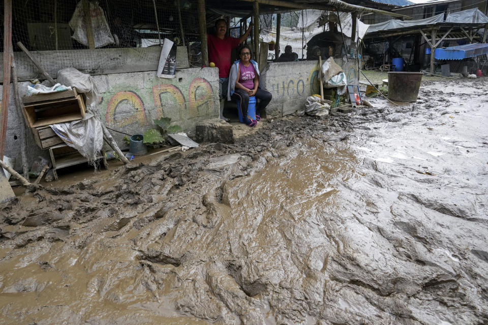 Residents sit in their houses along a road flooded by a landslide caused by heavy rains in Banos, Ecuador, Monday, June 17, 2024. (AP Photo/Dolores Ochoa)