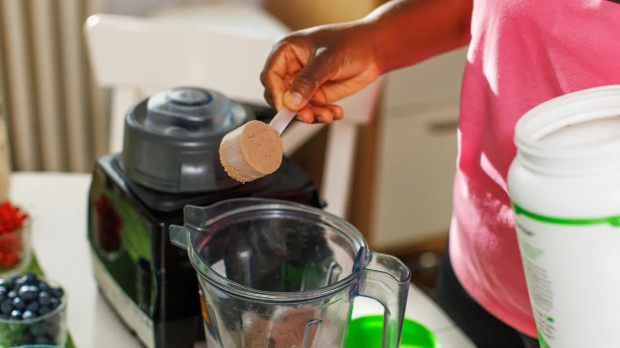  Person placing scoop of protein powder into a blender. 