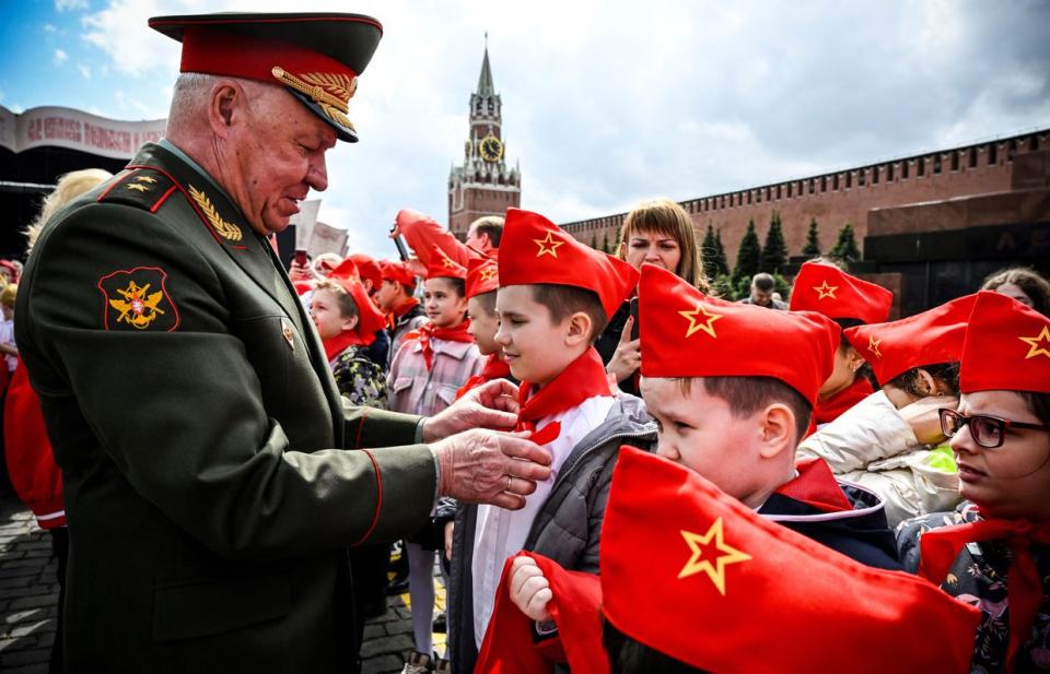 A Russian Army Lieutenant-General ties a red scarf around a child's neck to symbolise his initiation into the youth organisation 'Young Pioneers,' on Red Square in Moscow on May 21, 2023. (Photo by ALEXANDER NEMENOV/AFP via Getty Images)
