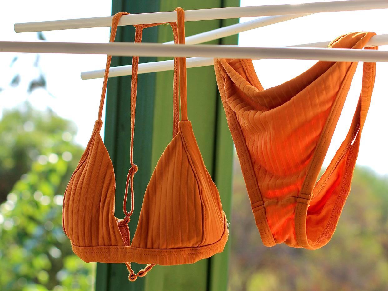 An orange bikini hanging out to dry in front of a green window.