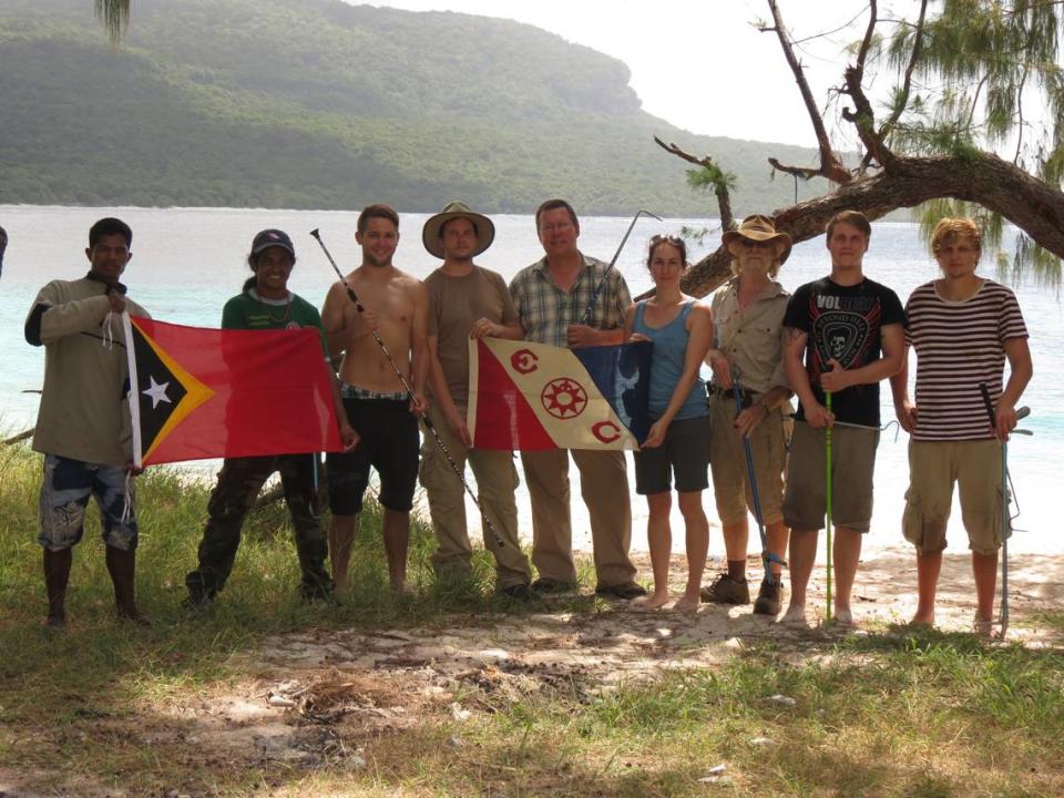 The research team poses with flags. From left to right, the photo shows an unnamed boatman and Agivedo “Laca” Varela Ribeiro holding a Timor-Leste flag, Mirco Wolfelschneider, Sven Mecke, Hinrich Kaiser, Laura Fuchs, Mark O’Shea, Lukas Hartmann, and Max Kieckbusch.