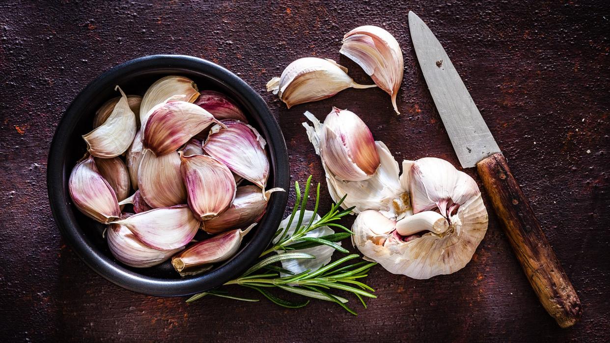 Vegetables: Garlic cloves in a black bowl shot from above on rustic brown background.