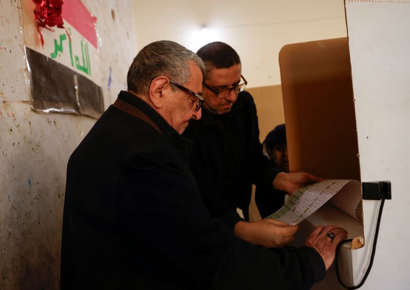 A relative helps an old Iraqi man as he votes during Iraq's provincial council elections, at a polling station in Baghdad