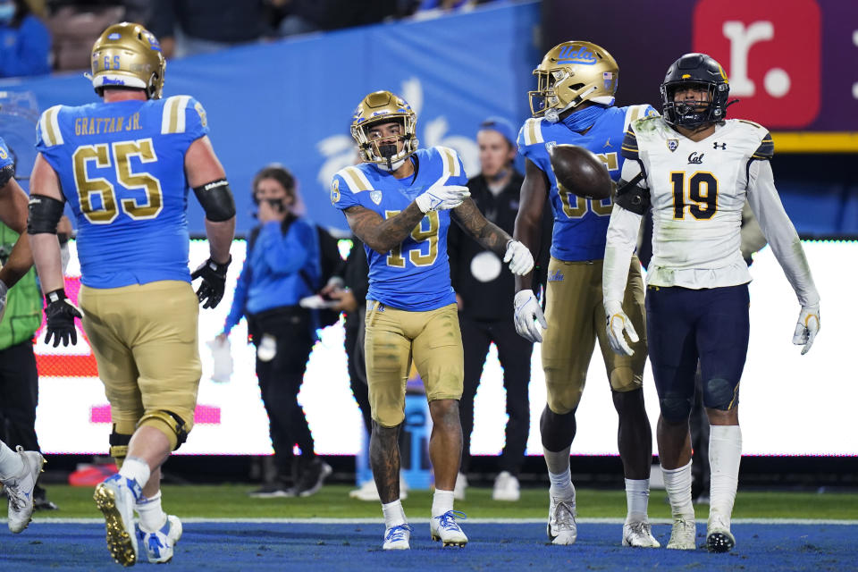 UCLA running back Kazmeir Allen, center, tosses the ball as he walks past California linebacker Cameron Goode, right, after scoring a touchdown during the first half of an NCAA college football game Saturday, Nov. 27, 2021, in Pasadena, Calif. (AP Photo/Jae C. Hong)