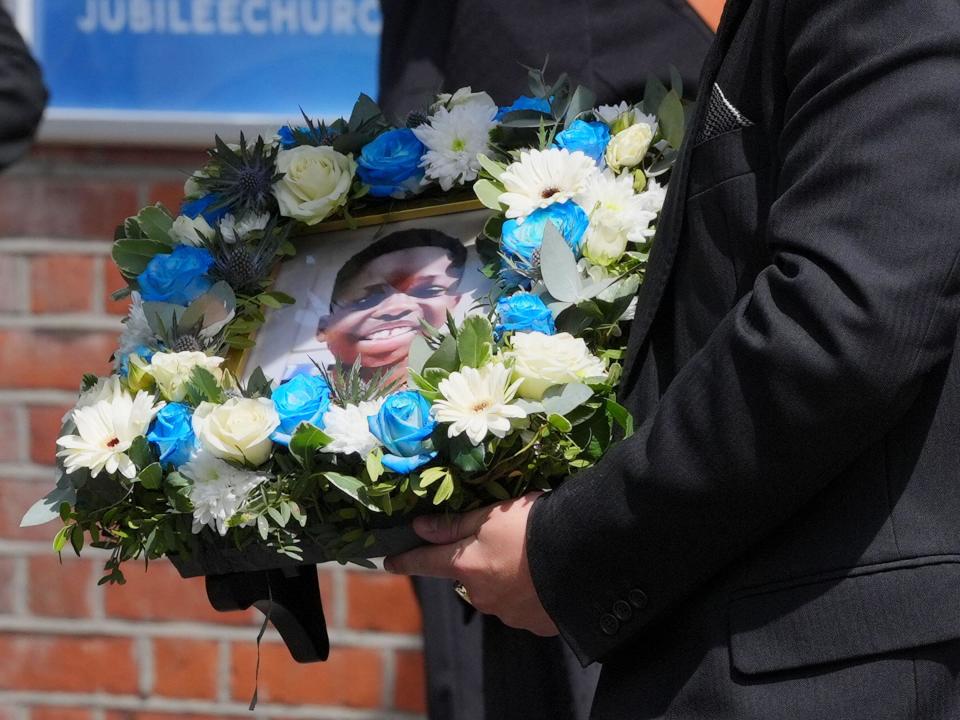 A funeral director carries a floral tribute inset with a photograph of Daniel Anjorin, 14, following his funeral service at Jubilee Church in Ilford, east London. The teenager died near his home as he walked to school in Hainault on April 30 in an attack which also left four people injured including two police officers. Picture date: Friday May 17, 2024.