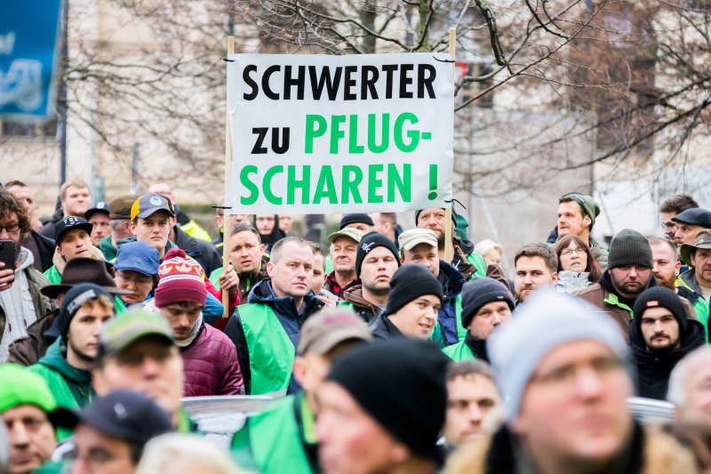 Participants hold a placard written "Swords to ploughshares!" during a poster organized by the Brandenburg State Farmers' Association against the increase in the tax on agricultural diesel in front of the federal office of Alliance 90/The Greens (Bündnis 90/Die Grünen). Farmers are demonstrating nationwide on Friday ahead of the budget debates in the German Bundestag next week. Christoph Soeder/dpa