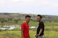 Joemar Flores, and his neighbor, Junthan Giumba pose for a photo with Flores' rice paddies visible in the distance in Mindanao, Philippines, May 9, 2024. A growing type of insurance, called parametric insurance, is helping farmers like Flores and others in developing countries respond to extreme weather events. (Bill Spindle/Cipher News via AP)