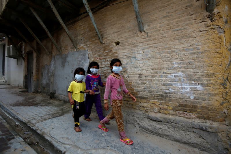 Iraqi children wear protective masks as they walk near a religious school where the first coronavirus case was detected, following the outbreak of the new coronavirus, in the holy city of Najaf