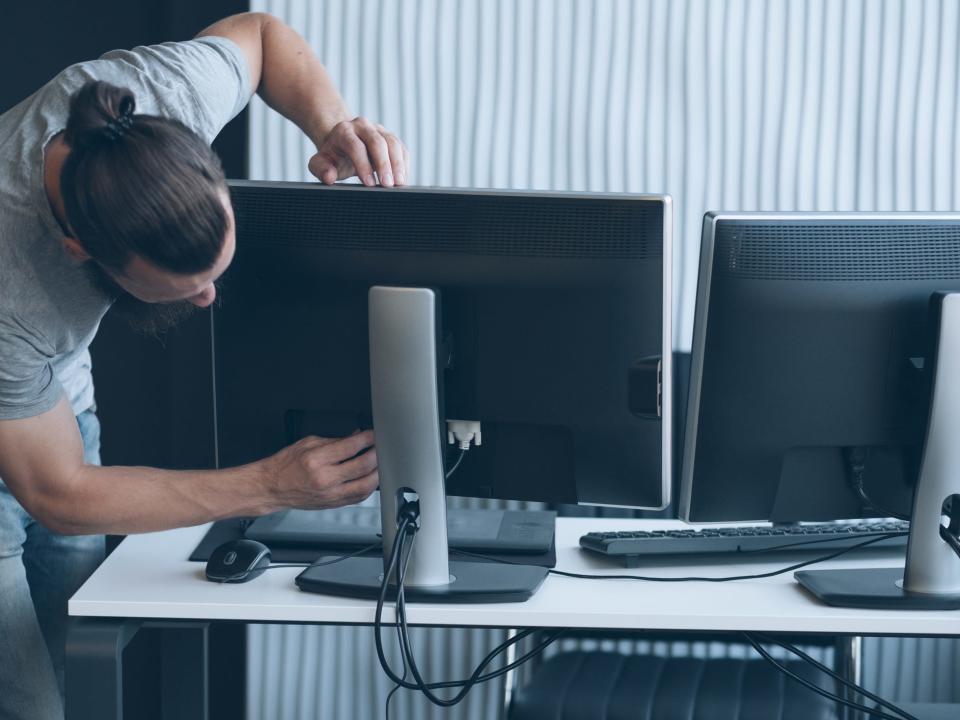 Man plugging cords into a computer monitor on a desk