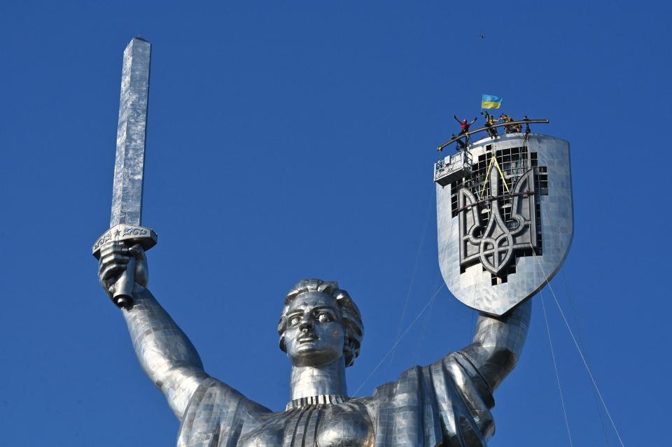 Steeplejacks wave a flag after they installed the Ukrainian coat of arms, replacing the coat of arms of the former Soviet Union, on the shield of the Motherland Monument in Kyiv, on Aug. 6, 2023.. The work came amid a campaign to remove Soviet icons that ramped up after Russia invaded Ukraine last year.