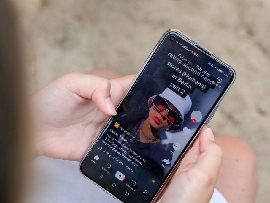 A girl is holding a smartphone in her hands, which shows a video on the TikTok app. (posed scene)