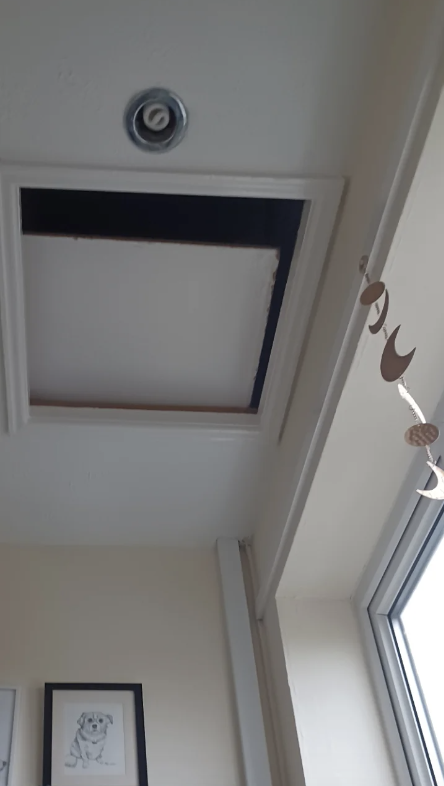 Ceiling with an open access panel and a hanging moon decoration near windows with a framed picture on the wall