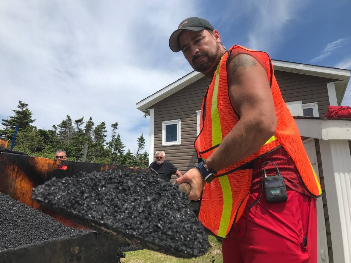 Peter English, owner of English's Paving, holds up a shovel filled with hot mix asphalt while paving a driveway in Bay de Verde this week. The company is paying considerably more for asphalt and diesel fuel this year. (Terry Roberts/CBC - image credit)