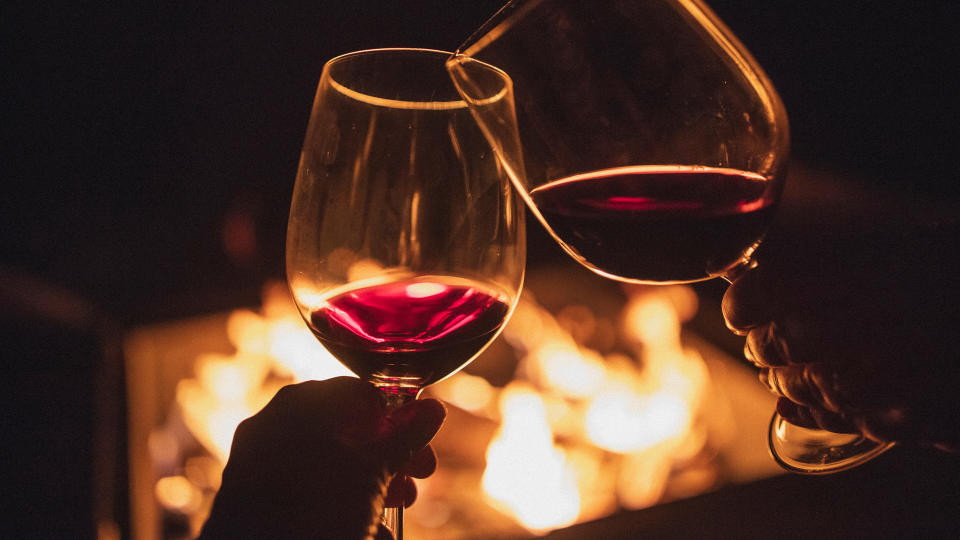 two people drinking red wine by a fire