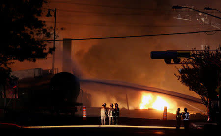 FILE PHOTO: Firefighters look at a train wagon on fire after a runaway train carrying crude oil derailed and exploded in Lac Megantic, Quebec, Canada, July 6, 2013. REUTERS/Mathieu Belanger/File Photo