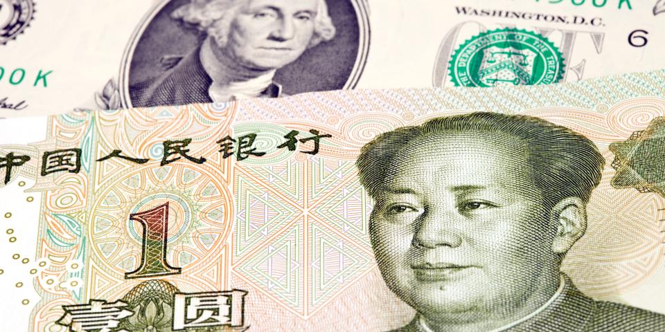 One Chinese yuan bill lying on top of a US dollar bill.