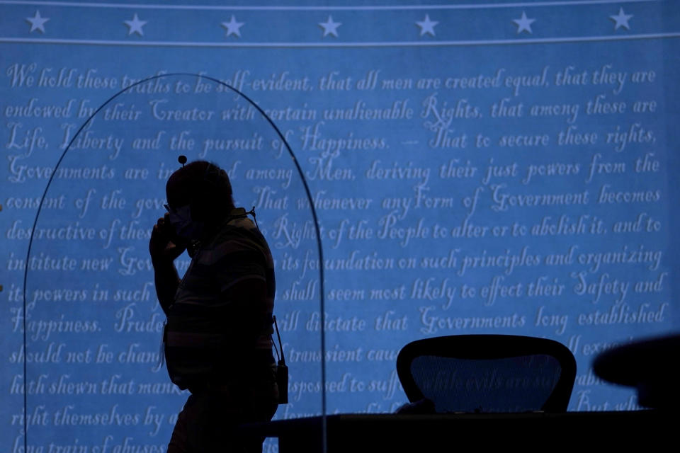 A member of the production crew walks behind a glass panel on stage which will serve as a barrier to protect the spread of COVID-19 as preparations take place for the vice presidential debate at the University of Utah, Tuesday, Oct. 6, 2020, in Salt Lake City. The vice presidential debate between Vice President Mike Pence and Democratic vice presidential candidate, Sen. Kamala Harris, D-Calif., is scheduled for Oct. 7. (AP Photo/Julio Cortez)