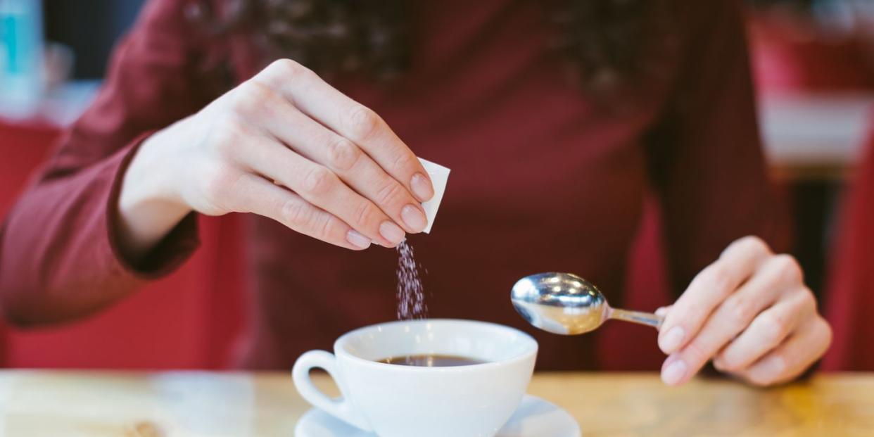 woman's hands pouring sugar into black coffee girl sitting at the table with espresso and smartphone blood and glycemic index control for diabetes excess of white sugar in food concept