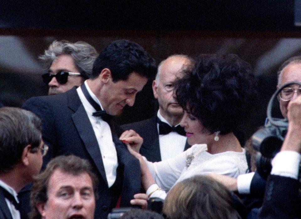 Elizabeth Taylor pins a red ribbon on Sylvester Stallone's tuxedo during the Cinema for Aids evening at the 46th Cannes on 20 May 1993 (Reuters)