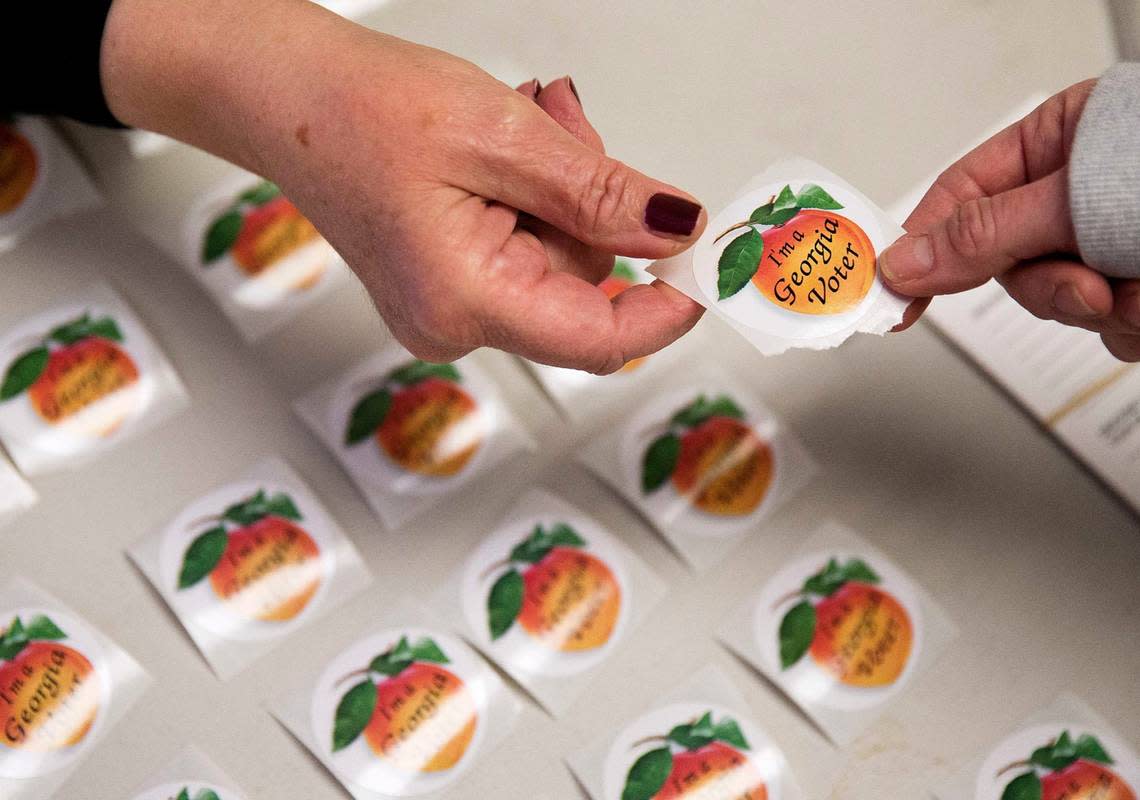 FILE - In this March 1, 2016 file photo, poll worker Delores Peterson, left, hands a sticker to a voter after they casted their ballot in Georgia’s primary election at a polling site in Atlanta. Georgians have a week left to vote early in primary runoff elections set for July 26. Secretary of State Brian Kemp’s office reports that more than 53,000 people cast ballots for races around the state since July 5. (AP Photo/David Goldman) David Goldman/AP