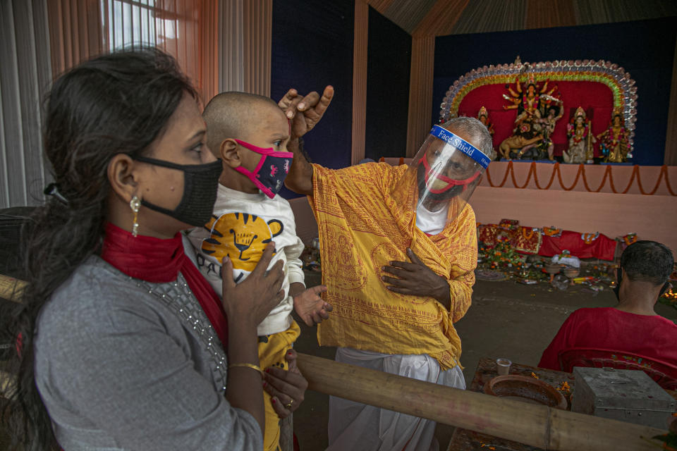 A Hindu priest wearing a face shield applies vermilion paste on the forehead of a child during Durga Puja festival in Gauhati, India, Saturday, Oct. 24, 2020. Weeks after India fully opened up from a harsh lockdown and began to modestly turn a corner by cutting new infections by near half, a Hindu festival season is raising fears that the disease could spoil the hard-won gains. Health experts worry the festivals can set off a whole new cascade of infections, further testing and straining India’s battered health care system. (AP Photo/Anupam Nath)