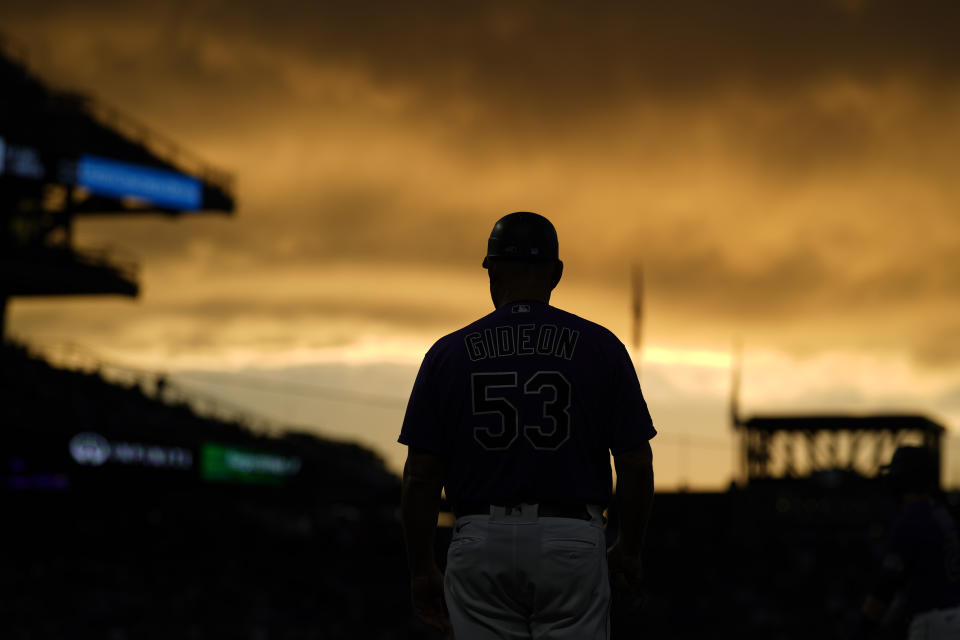 Colorado Rockies first base coach Ronnie Gideon stands on the field as the setting sun illuminates clouds during the third inning of the Rockies' baseball game against the Milwaukee Brewers on Saturday, June 19, 2021, in Denver. (AP Photo/David Zalubowski)