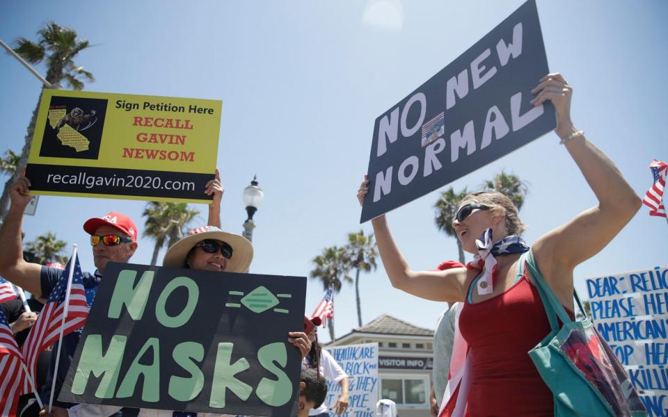 Demonstrators hold signs as they protest the lockdown and mask requirements in Huntington Beach, California - Marcio Jose Sanchez/AP